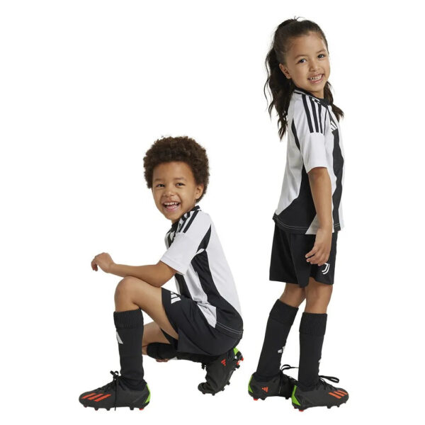 Two kids in matching black-and-white soccer uniforms posing against a white background; one crouching, one standing and smiling.