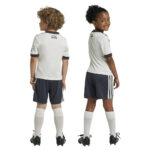 adidas-manchester-united-24-25-junior-third-set_1 | UAE SPORT STORE Two children in white and navy soccer uniforms, one facing away and one in profile, wearing white socks and black cleats.
