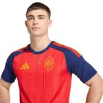 Portrait of a man wearing a Spain national football team jersey (red with blue sleeves), standing with hands on hips.