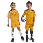 Two young children wearing yellow Real Madrid soccer jerseys stand side by side, one holds a soccer ball.