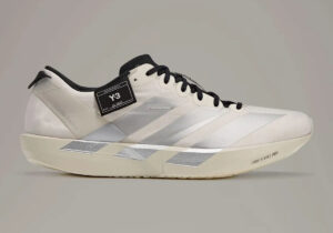 White sneaker with black laces and a black Y-3 tag on the side, featuring light gray chevron stripes and a cream sole marked LIGHTSTRIKE PRO.