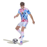Soccer player in a vibrant camo jersey, white shorts, and pink-striped socks dribbling a ball on a white background.