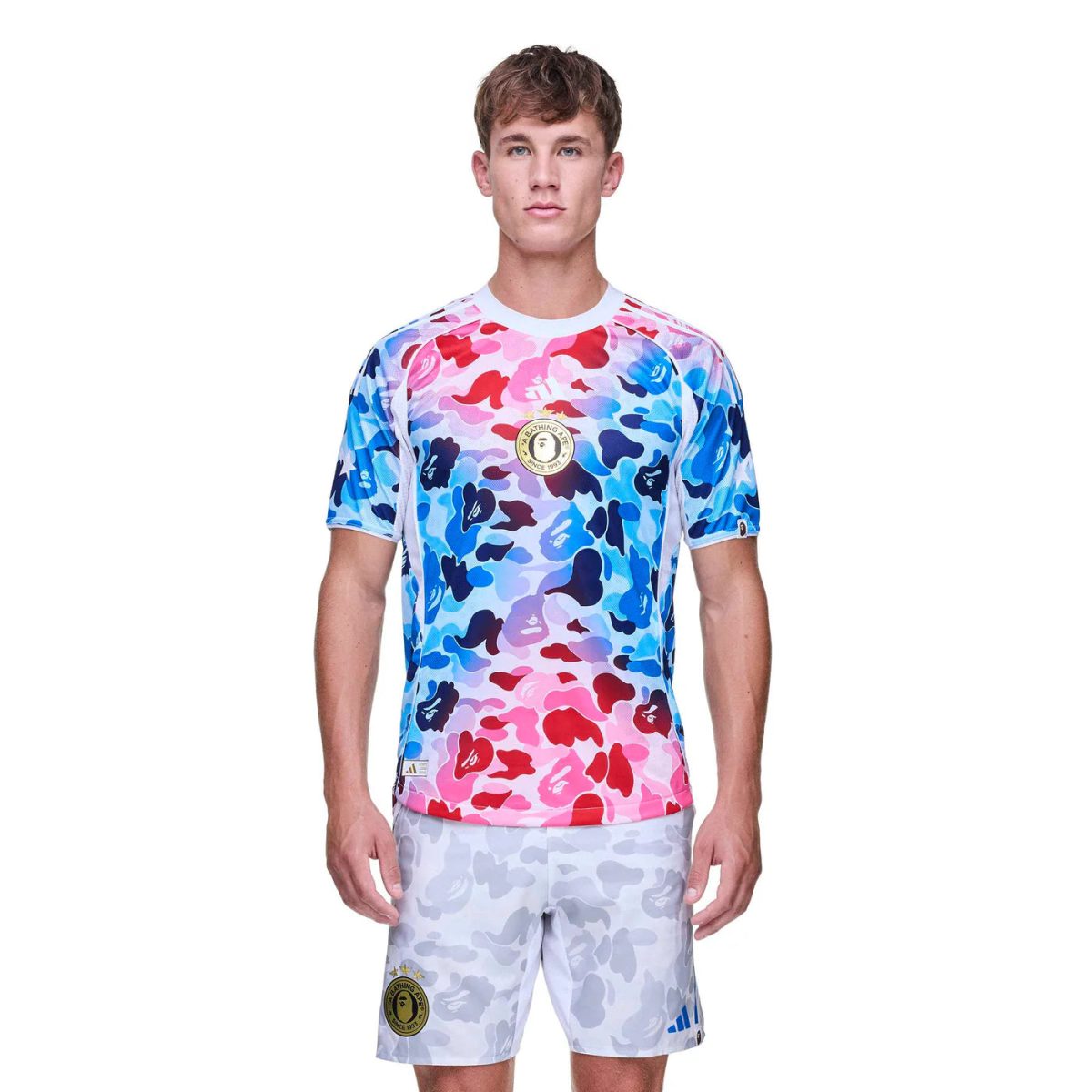 Man wearing a vibrant pink-to-blue camouflage short-sleeve athletic jersey with light gray camouflage shorts on a white background.