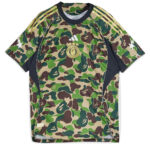 Camouflage-pattern athletic jersey with a round gold emblem at the chest and white Adidas-like stripes on the shoulders; short sleeves and dark trim around the neck and sides.