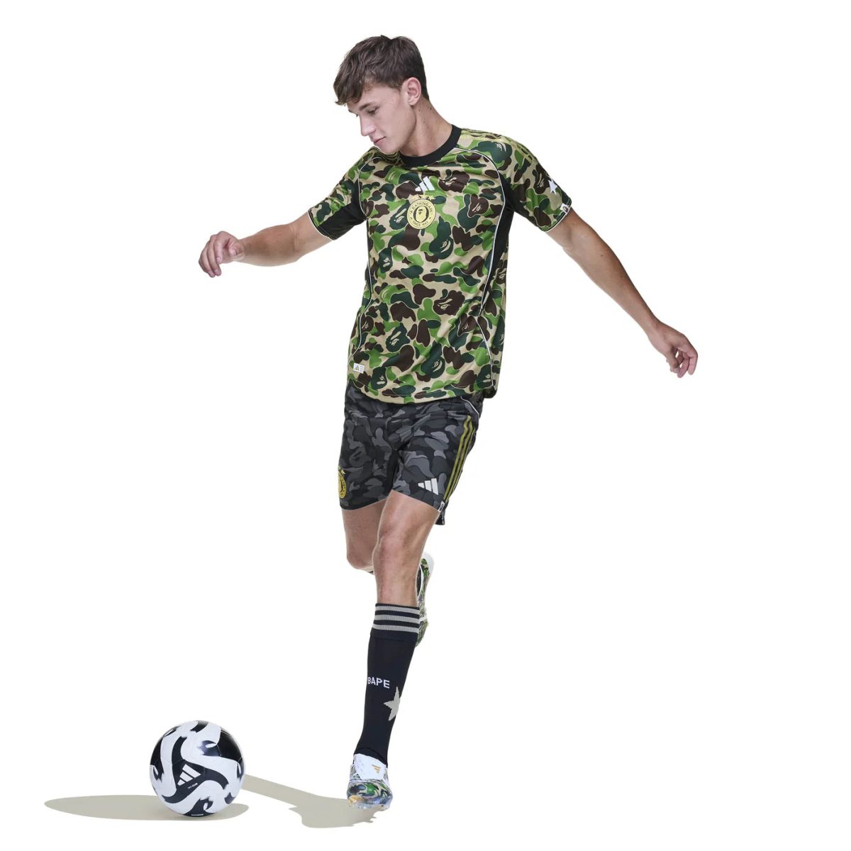 Male soccer player in camouflage kit dribbling a soccer ball on a white background.