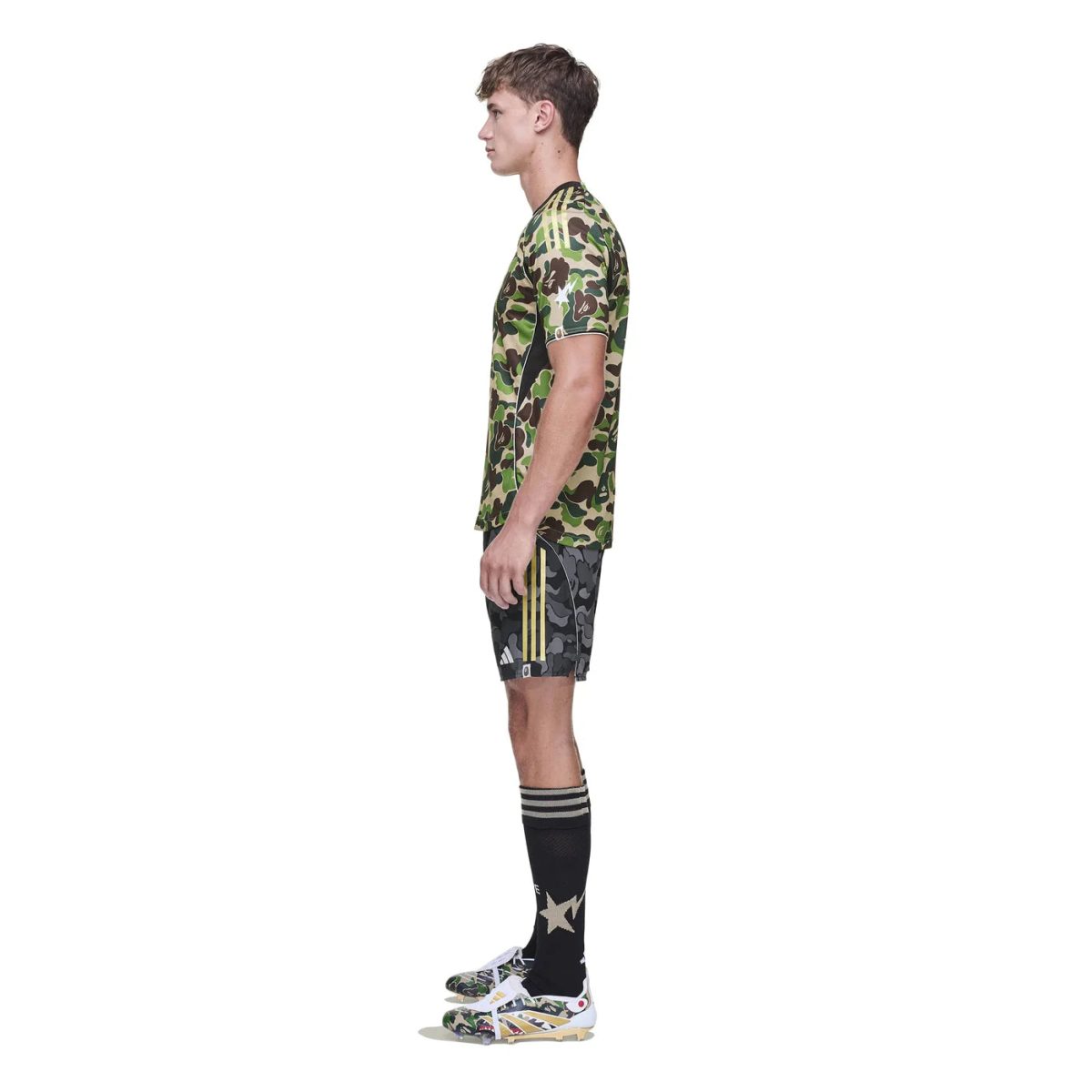Side view of a man in camouflage athletic outfit: camo T-shirt, camo shorts with yellow stripes, black knee-high socks, and camo sneakers.