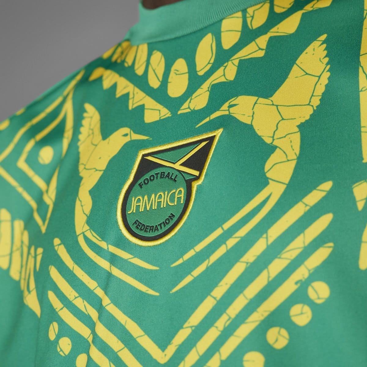 Close-up of the Jamaica Football Federation crest on a green jersey with yellow patterning.