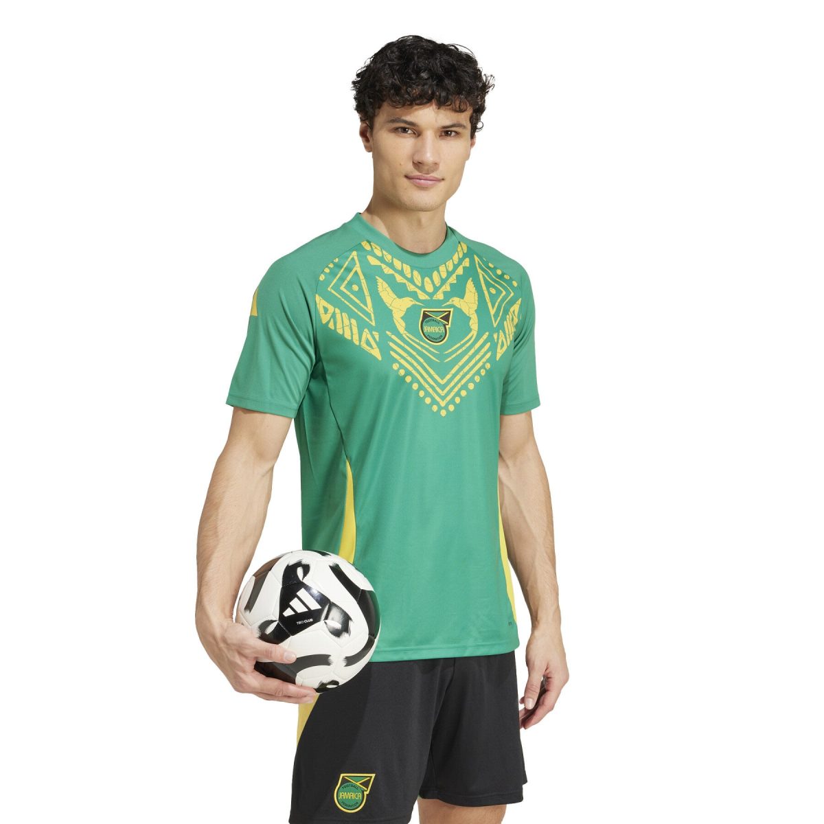 Young man in a green Jamaica soccer jersey holding a black-and-white soccer ball at waist level.