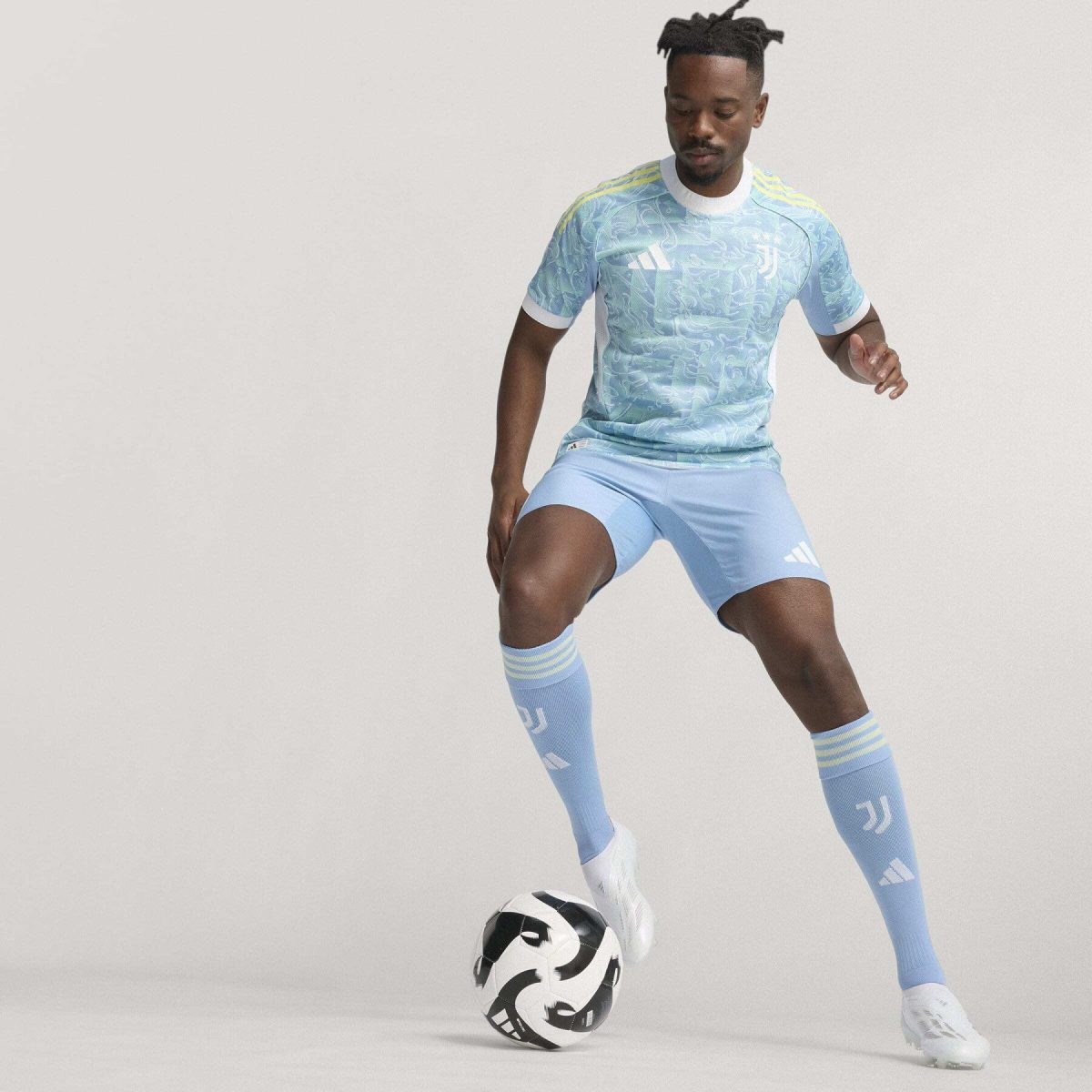 Soccer player in a light blue kit controls a black-and-white ball on a plain backdrop, mid-action.