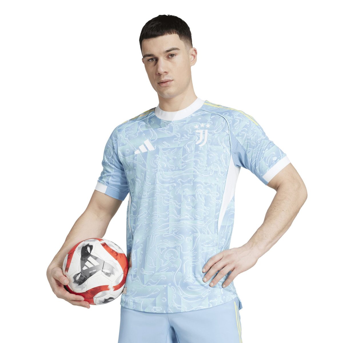 Young man in a light blue patterned soccer jersey holds a red-and-white soccer ball against a white background.