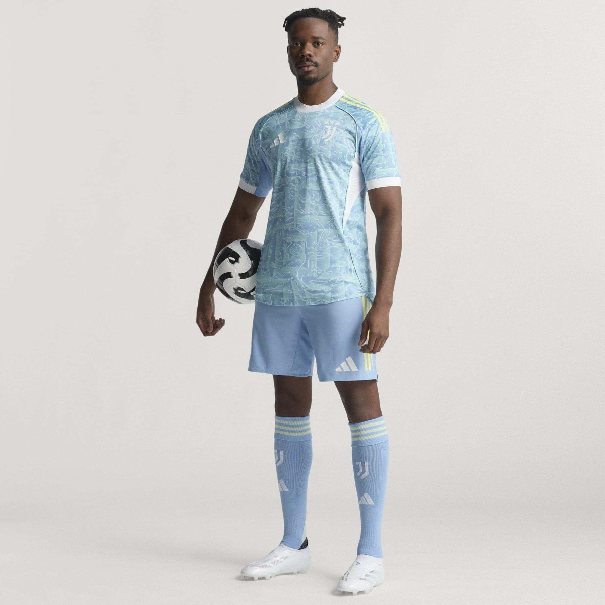 Soccer goalkeeper in light blue patterned jersey holding a black and white soccer ball, standing headset-ready pose with pale background