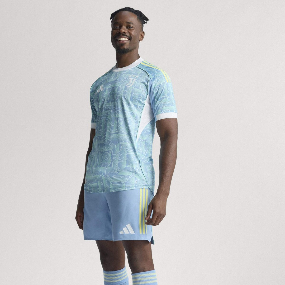 Smiling man in a light blue patterned soccer jersey and shorts, standing against a neutral background.