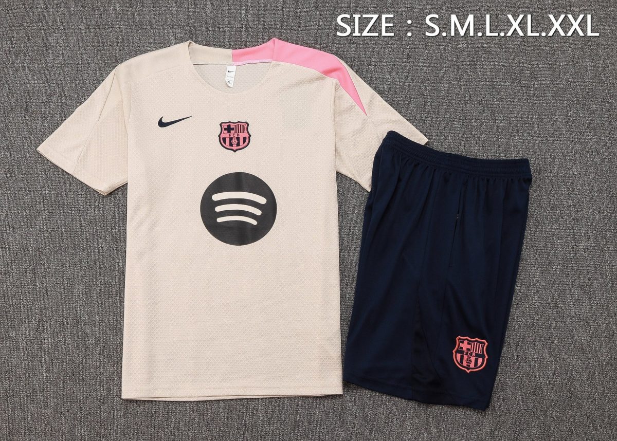 Beige FC Barcelona soccer jersey with pink shoulder detail, black Nike swoosh, club crest, and dark navy shorts with Barça emblem.