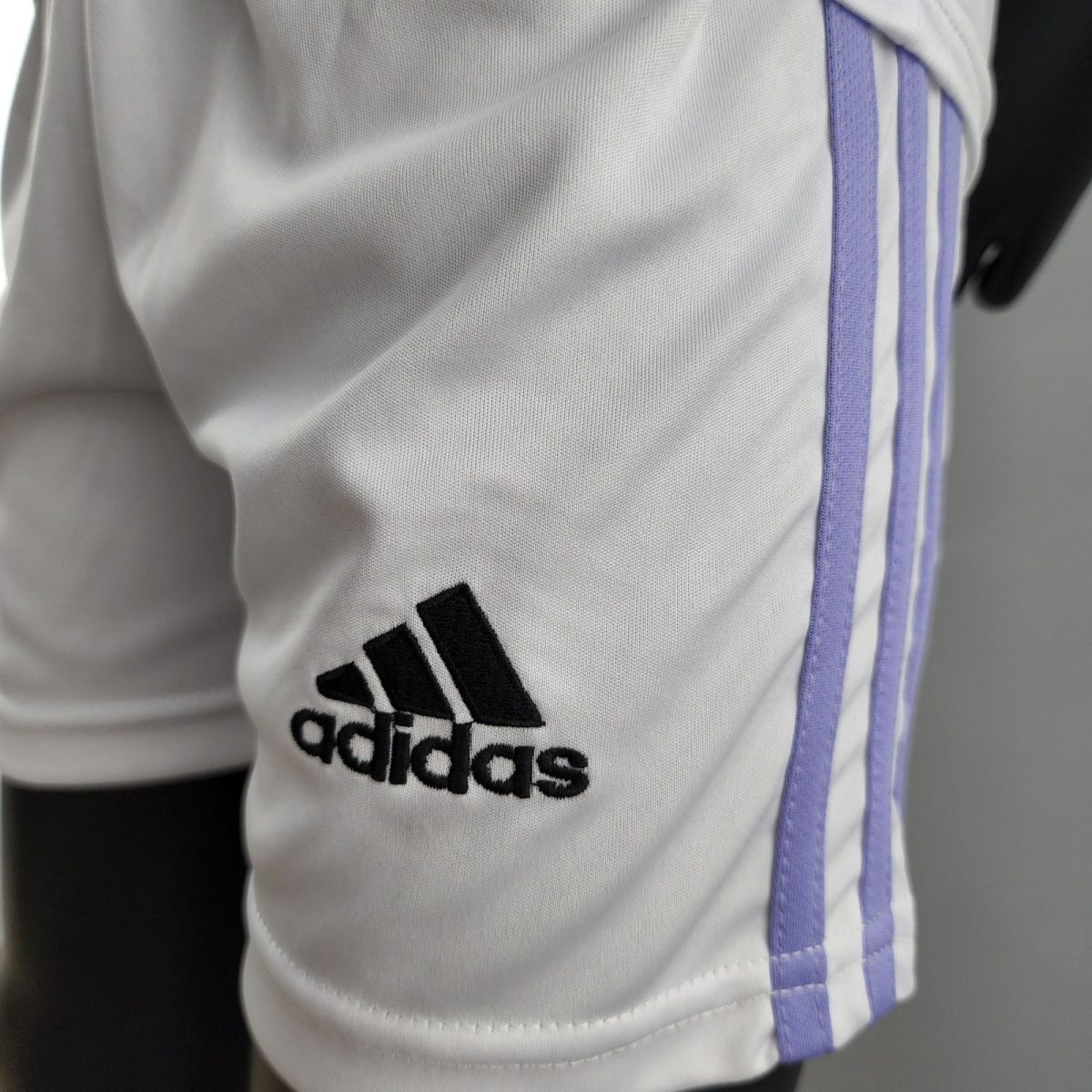 Close-up of a white Adidas sports jersey with purple vertical stripes and black logo close to the bottom left of the frame, partial view visible.