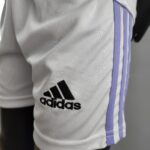 Close-up of a white Adidas sports jersey with purple vertical stripes and black logo close to the bottom left of the frame, partial view visible.