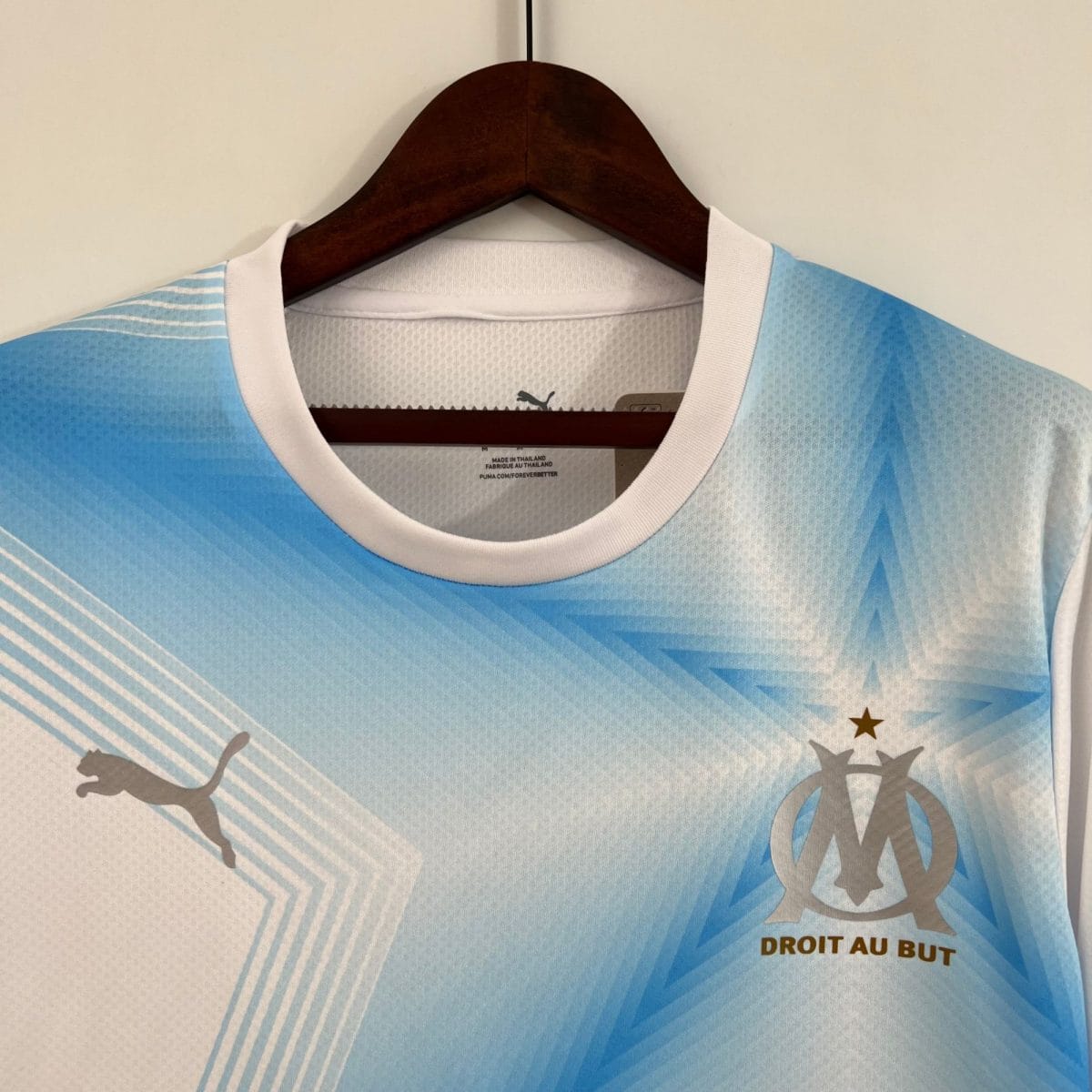 Close-up of a light blue athletic jersey on a wooden hanger with a white collar, hanging against a light wall.