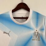 ae7101f3_f921e6ae-3844-40a6-9c98-6a8199d5f005 | UAE SPORT STORE Close-up of a light blue athletic jersey on a wooden hanger with a white collar, hanging against a light wall.