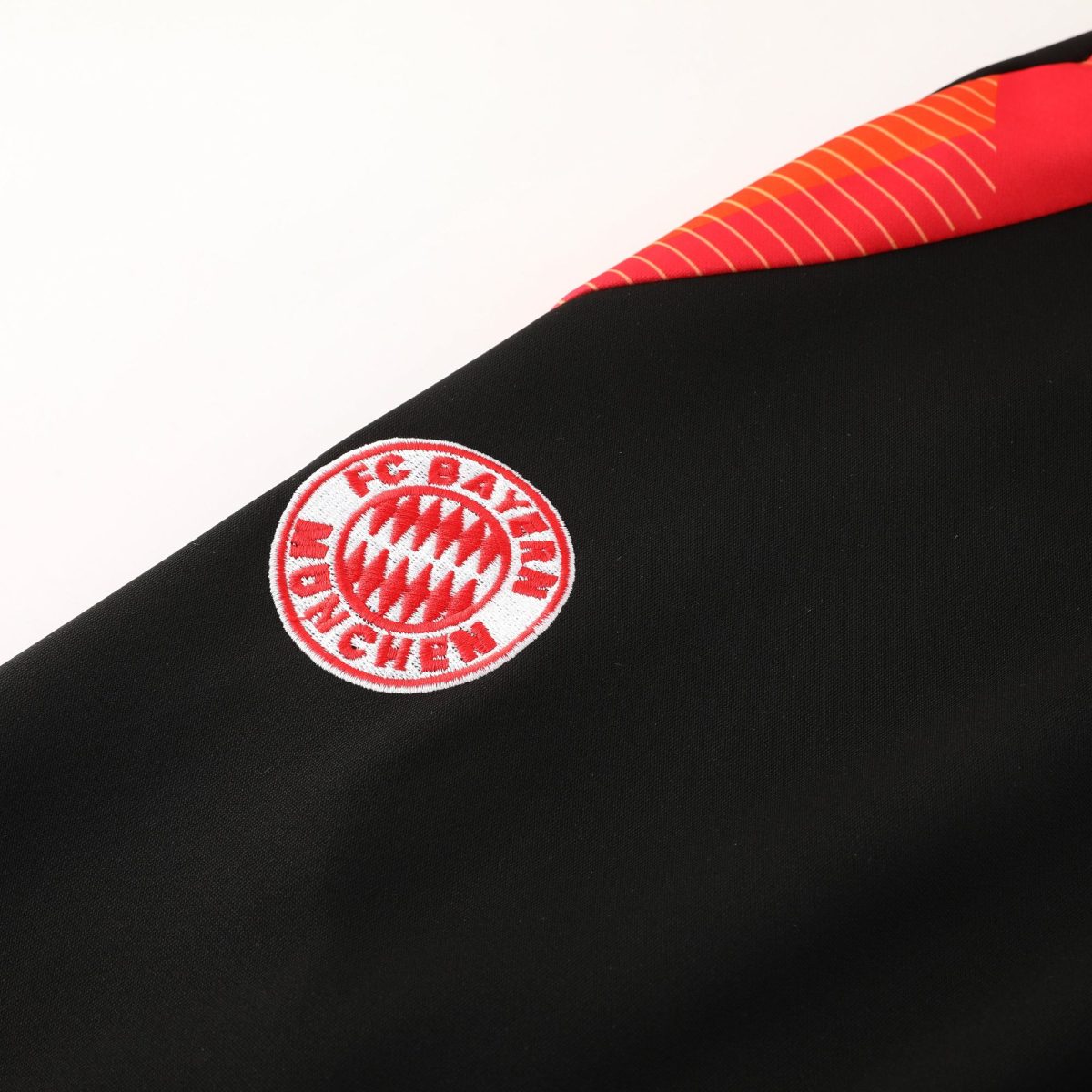 Close-up of a red-and-white Bayern Munich crest embroidered on black fabric, partially visible along a diagonal seam.