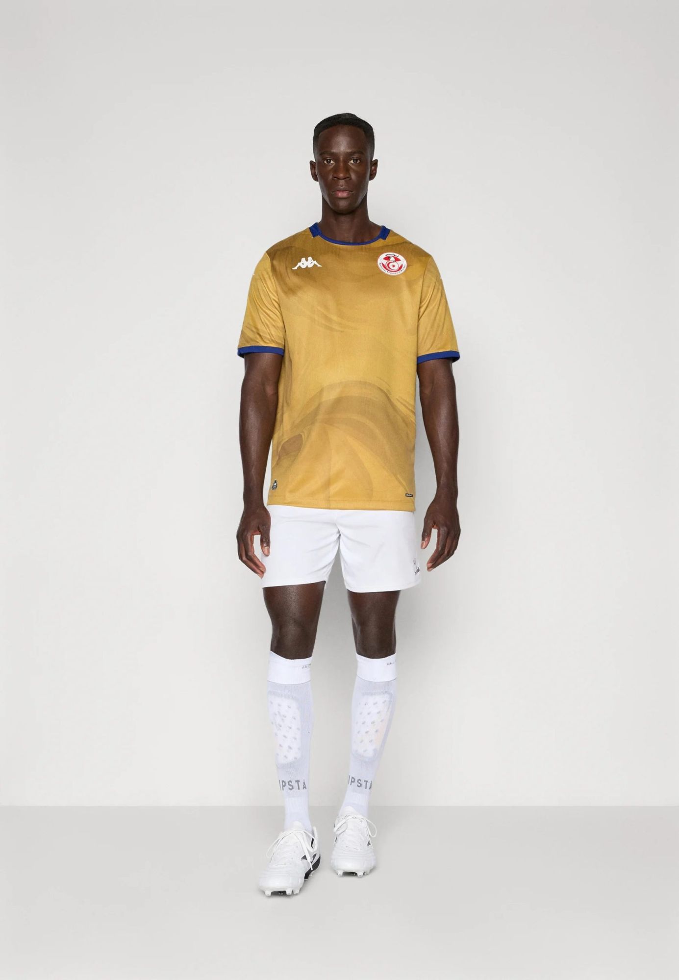 aef5817d0c3b4b21ac657eab90f214fc | UAE SPORT STORE Full-body shot of a male model wearing a gold soccer jersey with blue trim, white shorts, and white socks against a light background.