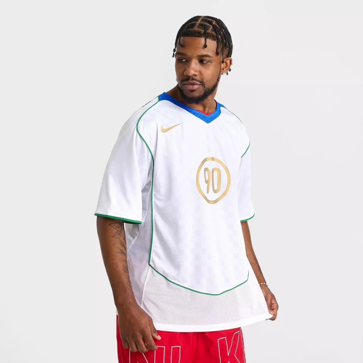 Male soccer player wearing a white jersey with gold 90 crest, blue collar, and green piping, standing against a light background.