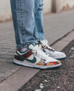 White sneakers with teal accents and camouflage panels, paired with blue jeans on a sidewalk.