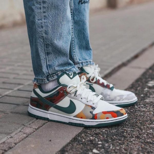 White sneakers with teal accents and camouflage panels, paired with blue jeans on a sidewalk.