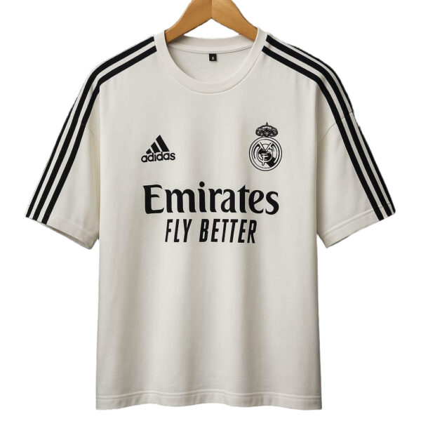 Cream Real Madrid football jersey with Adidas logo, club crest, and 'Emirates Fly Better' sponsor on front, hanging on a wooden hanger.