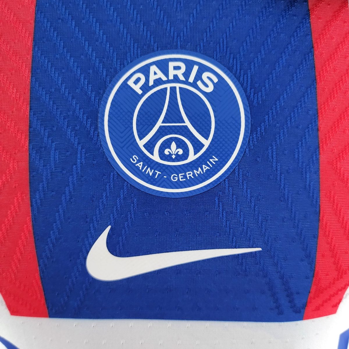 Close-up of the Paris Saint-Germain club badge on a blue jersey with red stripes and a white Nike swoosh nearby.