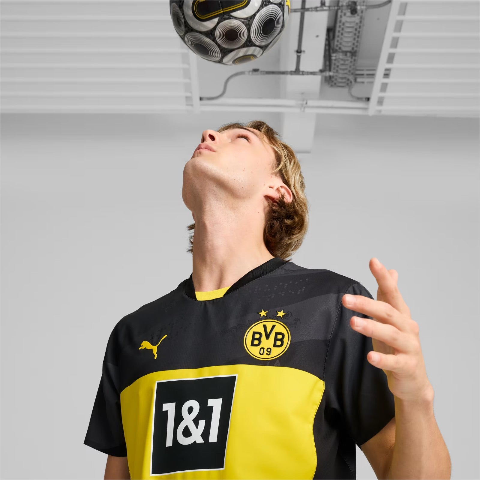 af95XqgxQl49j4n | UAE SPORT STORE Footballer wearing Borussia Dortmund jersey looks up at a patterned soccer ball overhead.