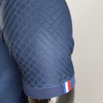 Close-up of blue fabric with a repeating diamond weave pattern and a red‑white‑blue stripe along the bottom edge.
