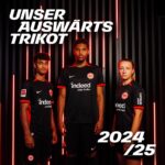 ag8p2lZMp6uzevL | UAE SPORT STORE Three players pose in black away kits with red trim against a dark striped backdrop with red neon accents, promoting the 2024/25 away kit (Unser Auswärts Trikot).