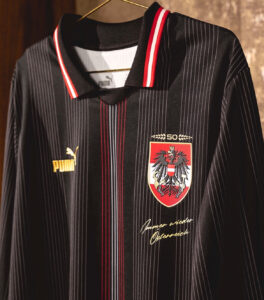 Black pinstripe Austria football jersey on a hanger, features a gold Puma logo, crest with eagle, and red-white-red collar trim.
