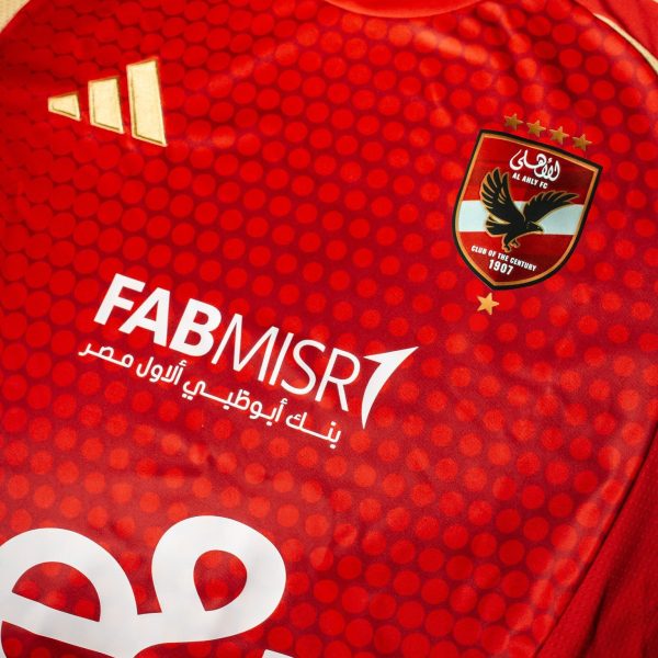 Close-up of a red Adidas sports jersey featuring the Al Ahly FC club crest, dotted pattern and white sponsor text