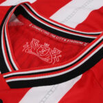 Close-up of a red sports jersey collar with black, white, and red striped trim; inner label reads 'CONNECTING THE CITY & STADIUM'.] ,