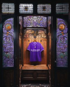 Purple sports jersey displayed in a wooden case with ornate stained-glass panels surrounding it.