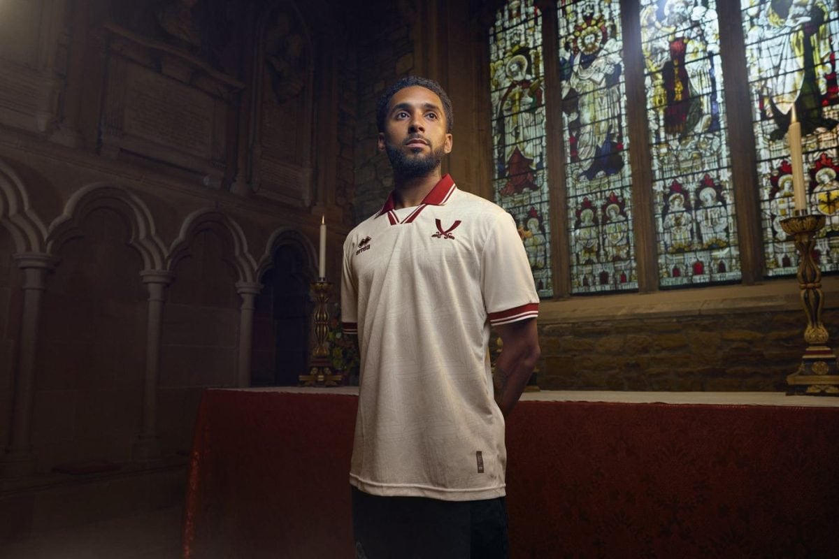Man in a white polo with red trim stands inside a church, near a red altar, with stained-glass windows behind him.