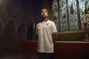 Man in a white polo with red trim stands inside a church, near a red altar, with stained-glass windows behind him.