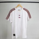 White pinstriped athletic jersey with maroon adidas three-stripe sleeves on a wooden hanger.