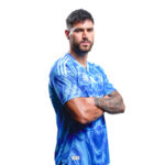 Man with a beard in a blue patterned sports jersey, arms crossed, looking at the camera on a white background.