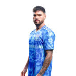 Man wearing a blue patterned sports jersey, looking to the side, white background behind him.