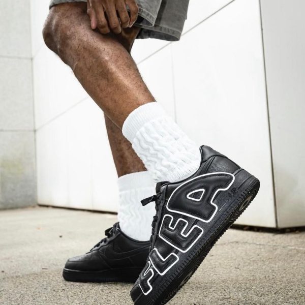 Person wearing black FILA sneakers with white detailing and large 'FILA' lettering, walking outdoors in white socks and gray shorts.