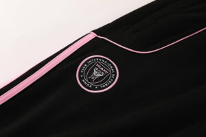 b05a39a6 | UAE SPORT STORE Close-up of black athletic jacket with pink piping and an embroidered circular logo behind the seam.