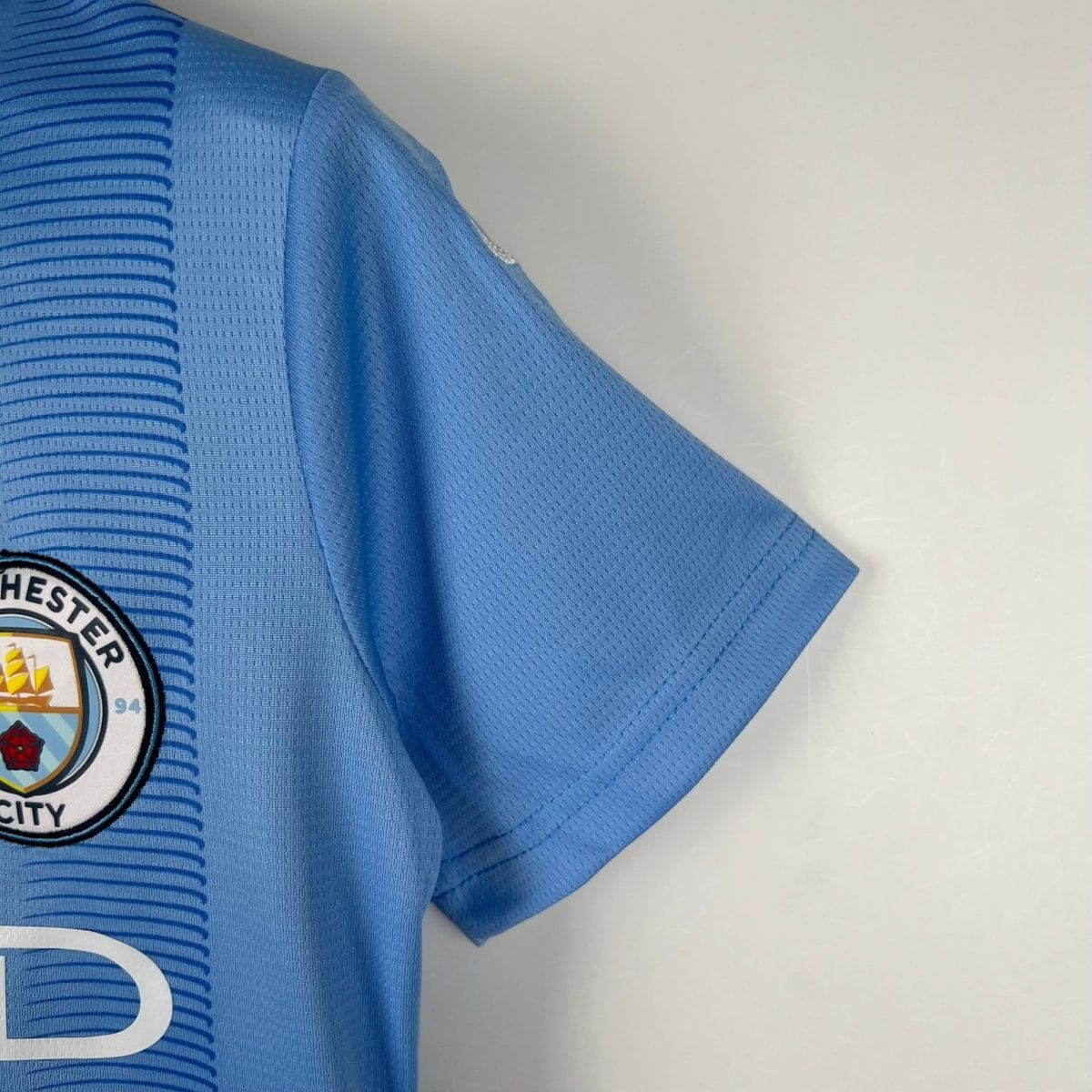 Partial view of a blue sports jersey with a circular patch on the lower left, showing white, yellow, and possibly shield elements.