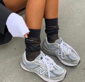 b0dad64b-6da2-4617-8b6b-ea3d5602400c_f3106786-4f3b-4d72-8331-016b1260fd00 | UAE SPORT STORE Gray New Balance sneakers with white laces on both feet, paired with black Prada socks, standing on a pavement.