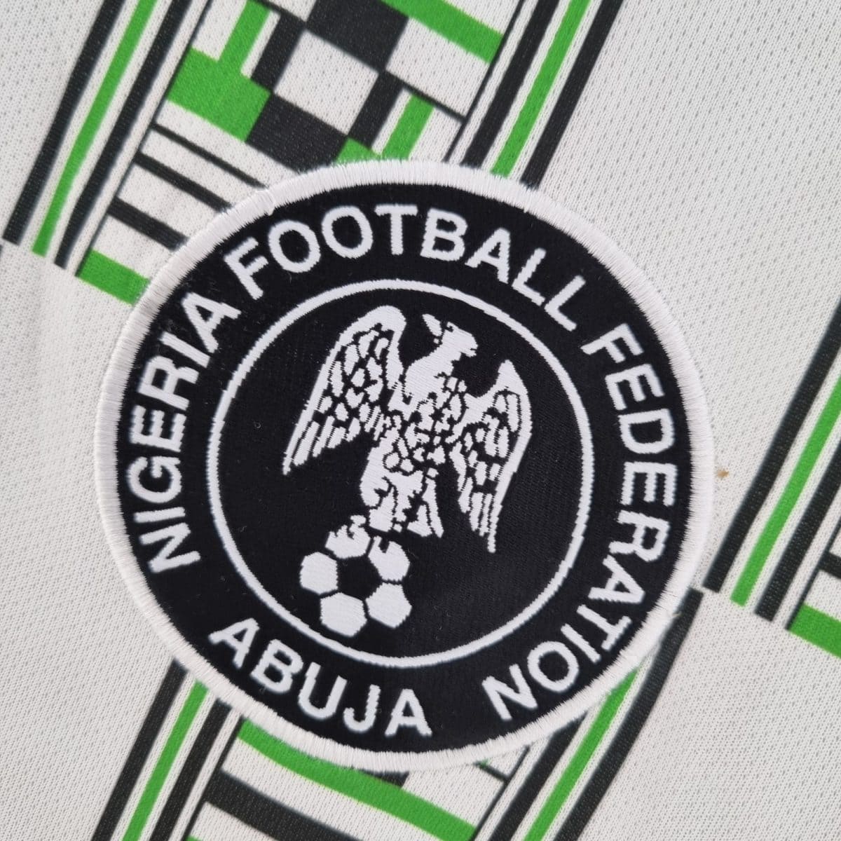 Close-up of a circular embroidered patch with black and white center and a bright green border, the word 'FOOTBALL' partially visible.