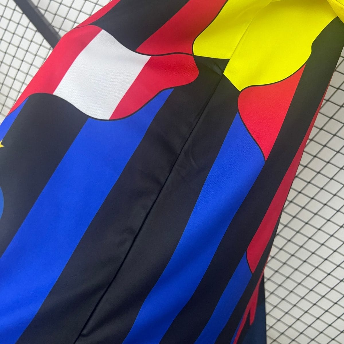 Close-up of a colorful abstract fabric design with bold red, blue, yellow shapes on black, photographed at an angle with a grid pattern in the background