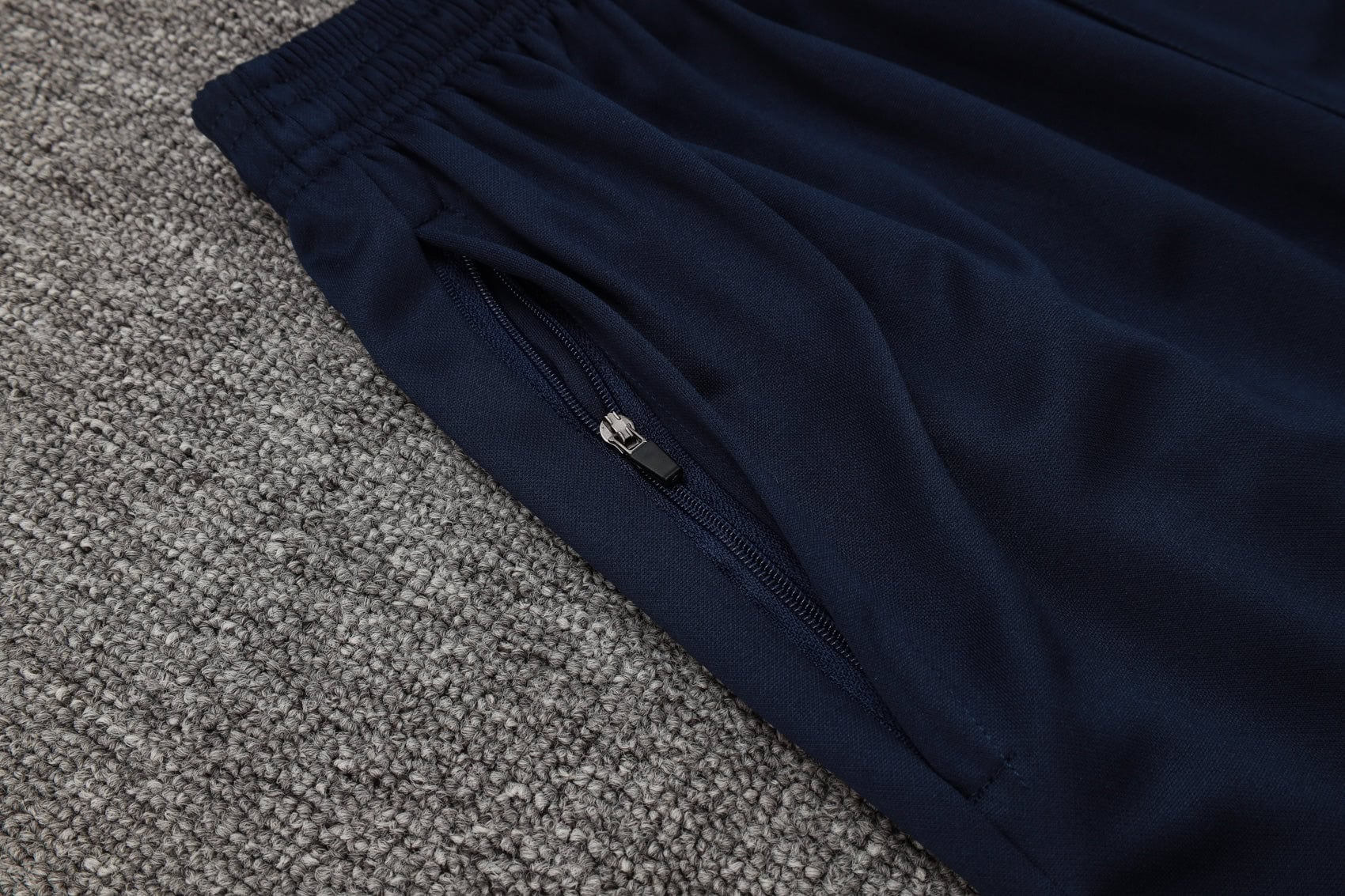 b16ef854 | UAE SPORT STORE Close-up of navy blue fabric with a zipper along a seam, lying on a gray carpet.