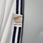 b1f3d17a_fc8eb008-93bc-401b-a9df-a04b7afa3a2d | UAE SPORT STORE White fabric with a dark blue stripe and a small tag reading 'REAL MADRID 1902-2002', suggesting a commemorative scarf or ribbon.
