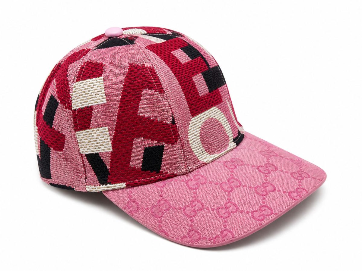 Pink Gucci baseball cap with a geometric red, black, and white crown and a pink brim with Gucci pattern on the underside and top edge.