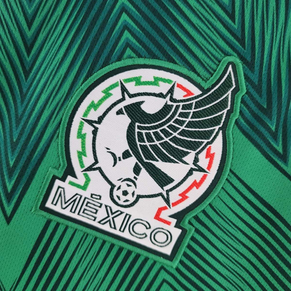 Close-up of green fabric with a textured chevron pattern and a white circular embroidered patch partially visible in the corner.